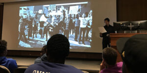 Ben Greenberg standing next to a PowerPoint presentation.