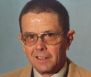 A headshot of a person wearing a tan suit.