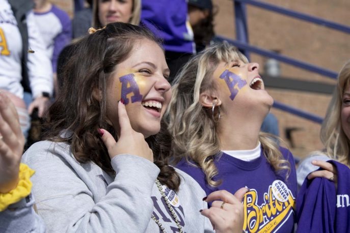 Two Albion College students in the bleachers with their faces painted.