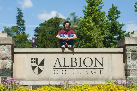 Anh Dinh posing on the Albion College campus sign