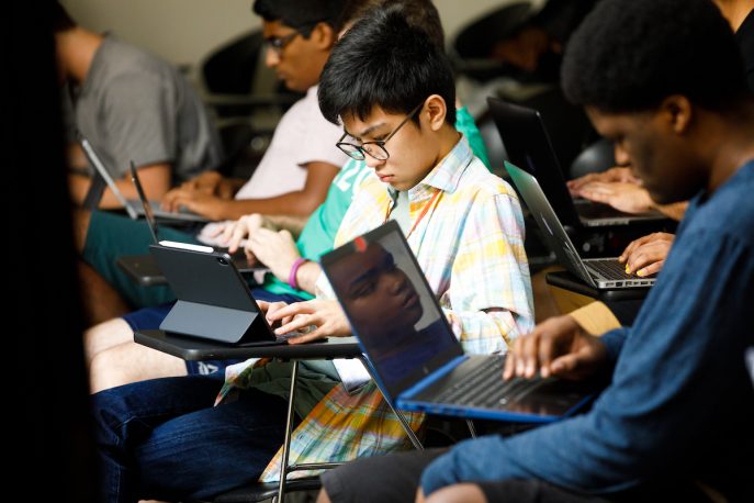 Students working on laptop computers in a classroom setting.