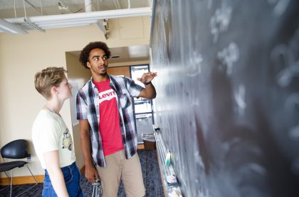 Two Albion students discussing writing on chalkboard.