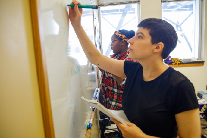 Two students working together and writing on a whiteboard