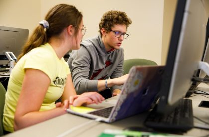 Two students discussing work in a computer lab.