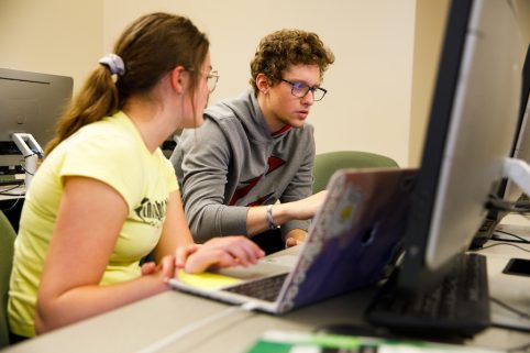 Two students discussing work in a computer lab.