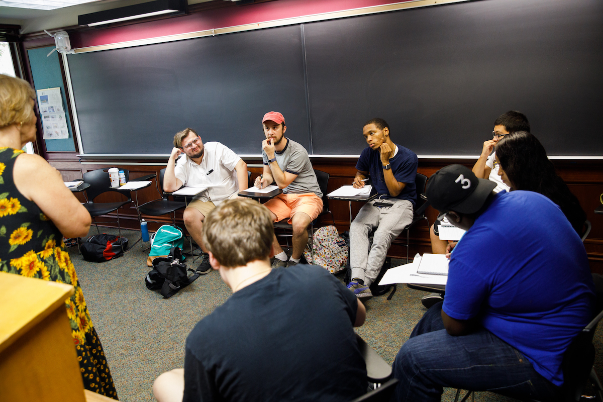 Faculty member conversing with a group of students in a classroom setting.
