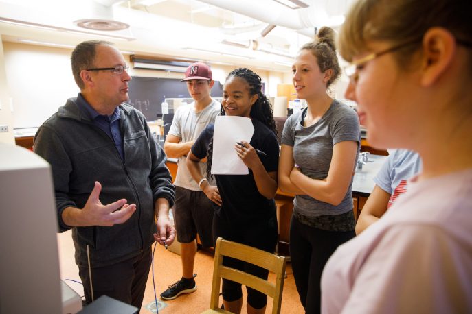 Faculty member conversing with a group of students in a classroom setting.