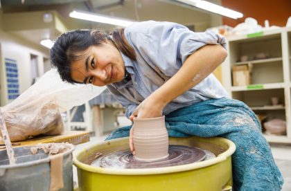 Student throwing pottery on a wheel in an art studio