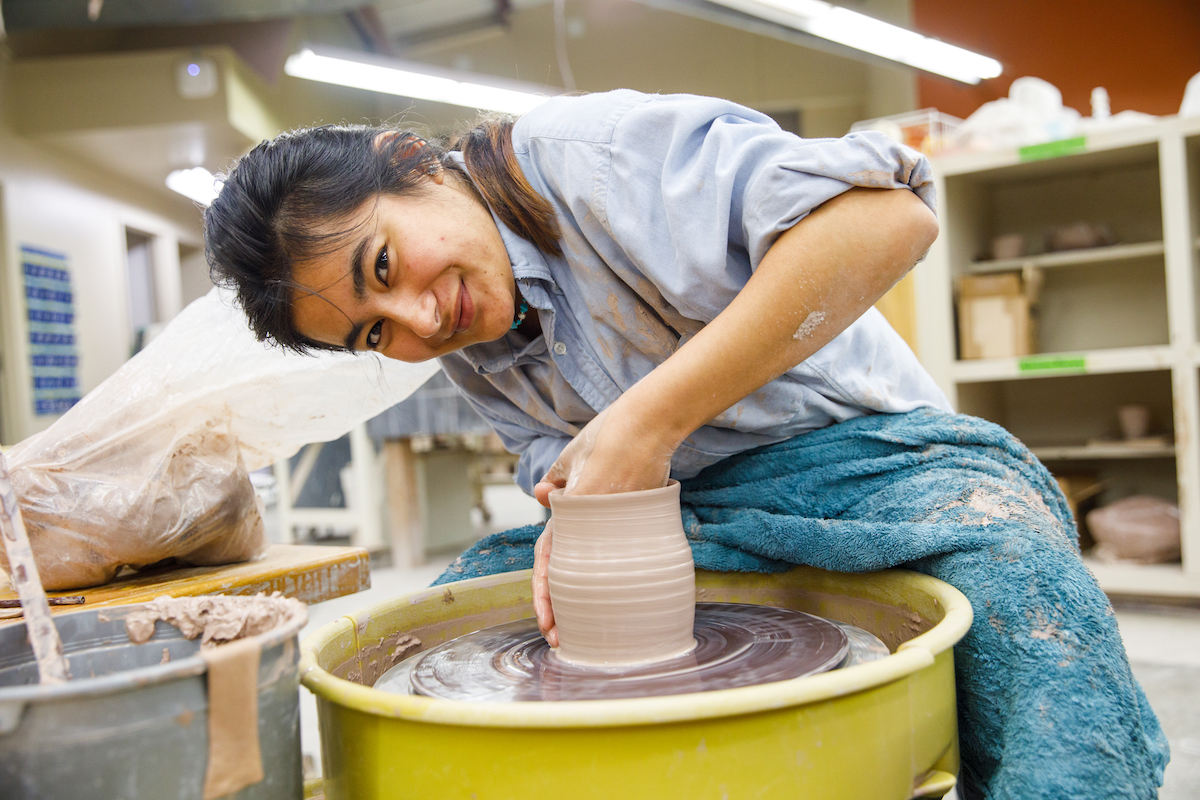 Student throwing pottery on a wheel in an art studio