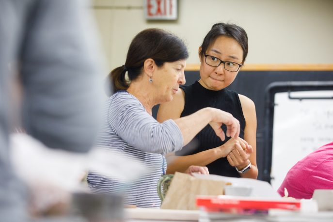 Faculty member converses with student in a pottery studio.