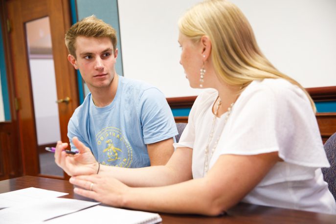 Student conversing with a faculty member in a classroom setting.