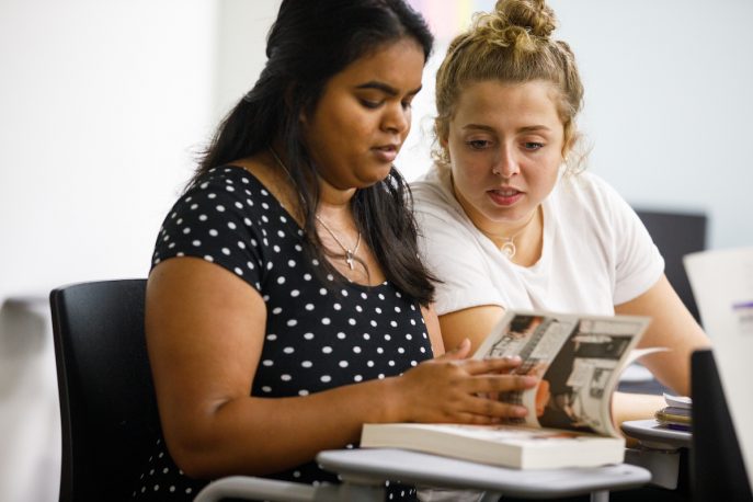 Two students sitting together reading a book together