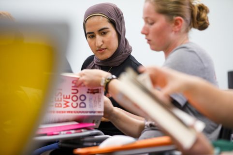 Two students discussing a book with one another