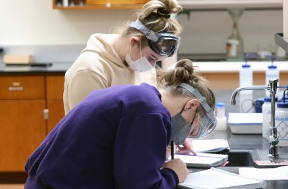 Two students in masks and goggles working in a lab