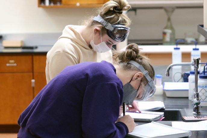 Two students in masks and goggles working in a lab