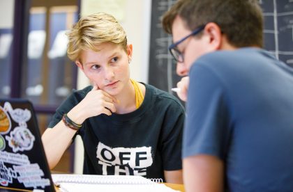 Two students having a discussion around a laptop computer.