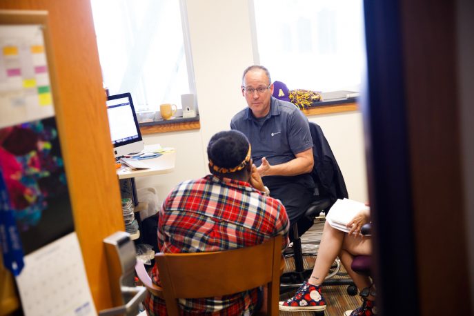 Faculty member conversing with two students in an office.