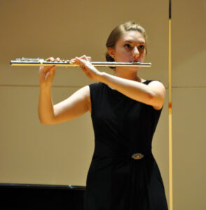 A female student wearing a black dress, playing the flute.