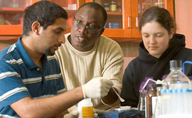 Two students and a professor sitting at a lab table.