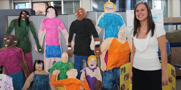 A female student standing next to hand painted life-size cutouts of people.