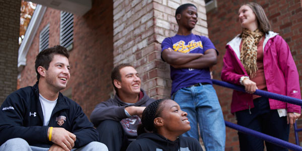 Five students outside Baldwin Hall. The three on the left are sitting on the steps, the two on the right are standing behind them.