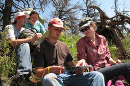 Four students sitting in the grass on a hill.