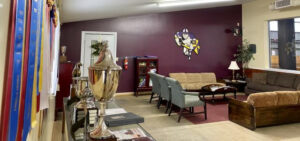 Shot of a room with couches and chairs. Trophies and ribbons are on display on the left wall.