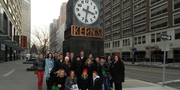 A group of students wearing coats standing in front of a giant clock that says "Kern's" on it.
