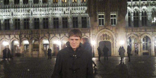 A student wearing a coat standing in front of a building at night.