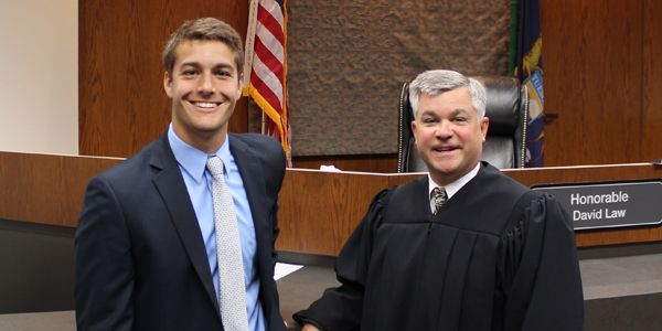 A student in a suit standing next to a judge in his robes.