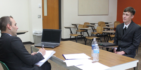A student wearing a suit sits across the table from a professor.