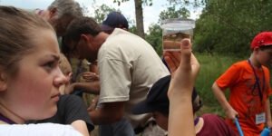 A group of students is gathered outside. One of them holds up a specimen cup.