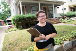 A student holding a clipboard standing in front of a house.
