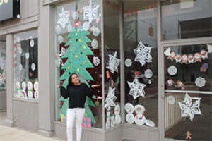 A student standing in front of a storefront decorated for Christmas.