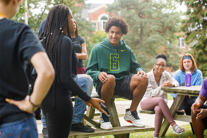 Students on the Quad sitting and standing near a picnic table.