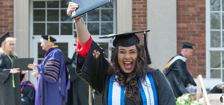 A student smiling and holding up her diploma cover.