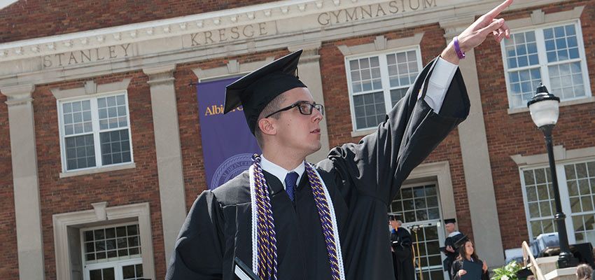A student in cap and gown pointing into the distance.