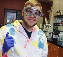 A student wearing safety goggles and gloves.