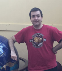 A student wearing a T-shirt leaning against a globe.