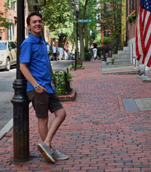 A photograph of a person leaning against a light pole. They are standing on a brick sidewalk.