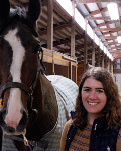 A student standing next to a horse.