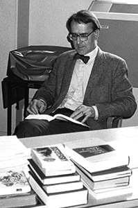 Black and white photograph of Dr. Gillham sitting at a desk looking at a book.