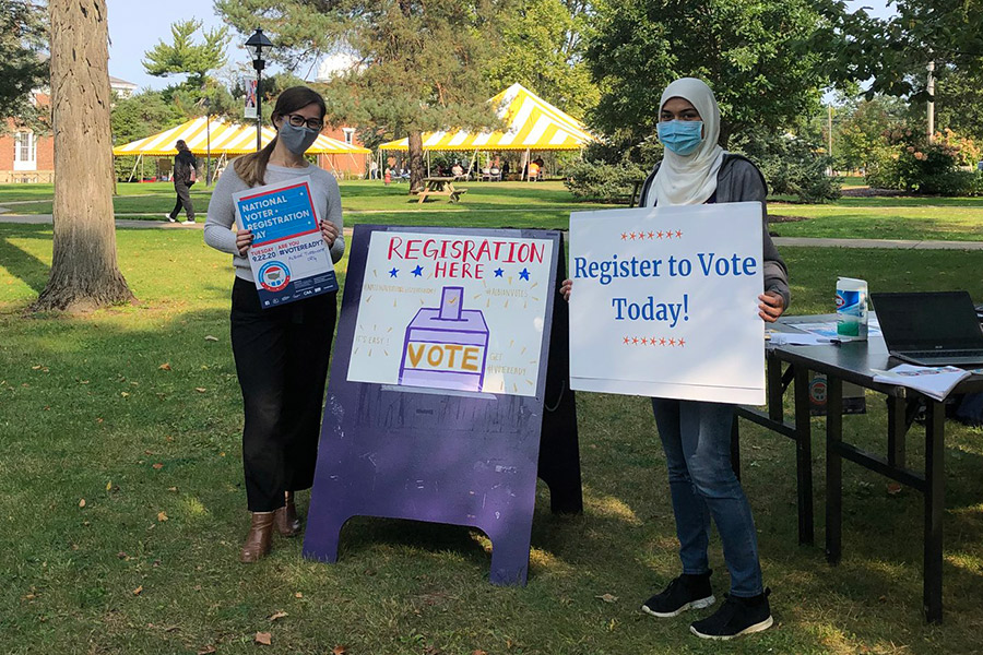 People standing next to a sign registering people to vote.