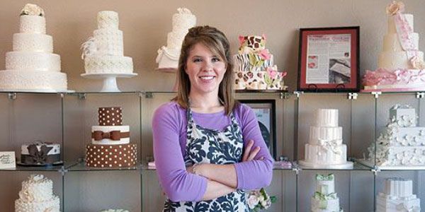 Kelly is standing in front of a display of wedding cakes.