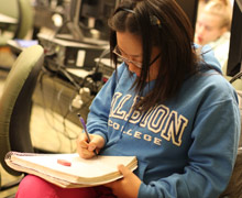 Student wearing Albion sweatshirt, writing in a notebook