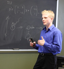 Math student giving a presentation in front of a chalk board.