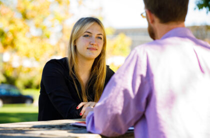 Two people sitting at a table talking to each other.