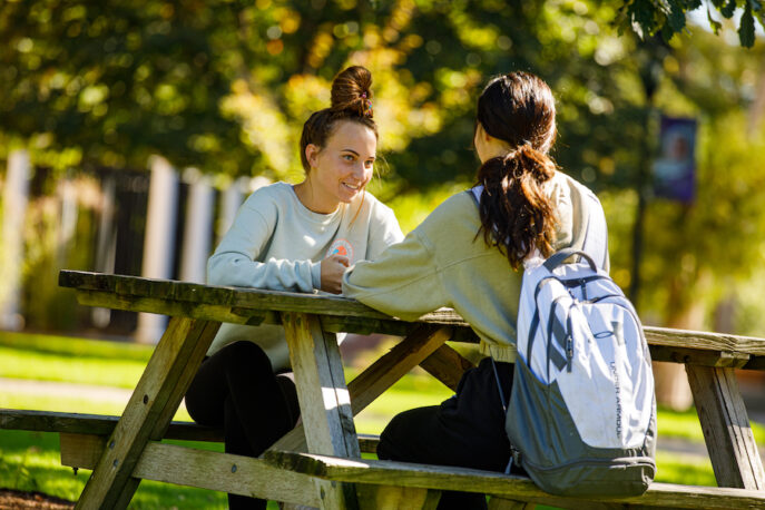 Two students in conversation at a picnic table.