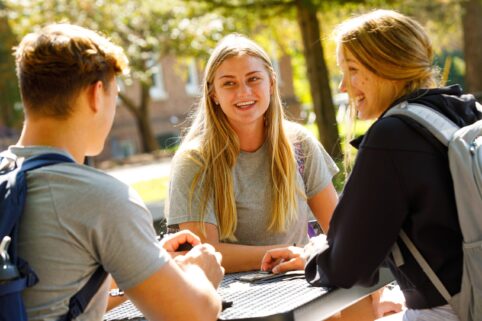 Students laughing together at a picnic table outside.