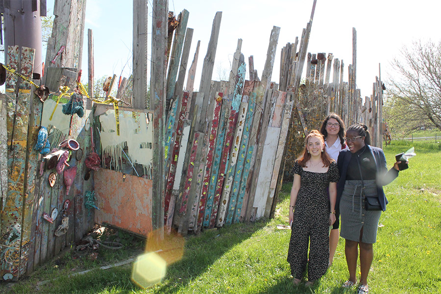 Albion College students posing next to a fence covered in artwork.